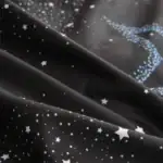 Tissu noir avec motifs d'étoiles blanches et bleues, évoquant un ciel étoilé ou une galaxie, parfait pour la décoration ou la couture créative.