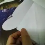 Pliage d'un bateau en papier blanc, tenu par une main, avec un fond de tissu à motif galactique. Idéal pour décoration ou activités éducatives sur l'espace et l'origami.