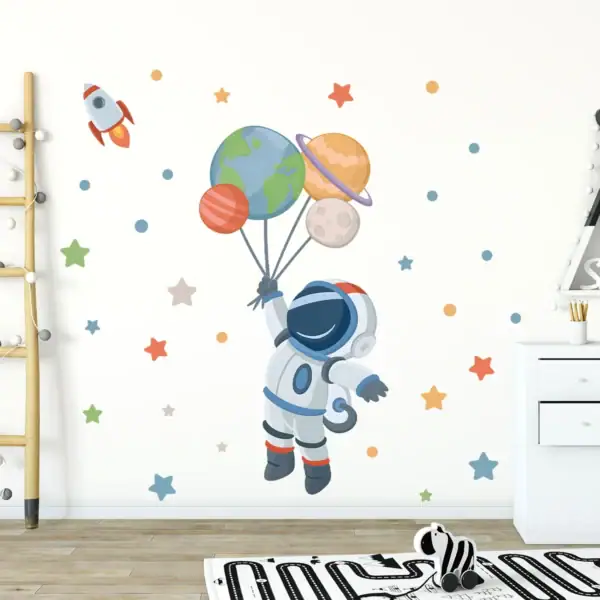 Un astronaute en costume spatial flotte dans un décor de mur avec des planètes en ballon, étoiles et fusée, créant une ambiance ludique et éducative sur le thème de l'espace.