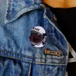 Pin's original en forme de chien portant un casque d'astronaute avec inscription "CCCP", fixé sur une veste en jean bleu, style décontracté.