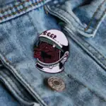 Pinceau en métal avec logo soviétique représentant un ours en costume d'astronaute, placé sur une veste en denim. Accessoire original pour les amateurs de science et d'histoire spatiale soviétiqu.
