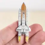 Pin's en forme de vaisseau spatial avec dĂ©tails en mĂ©tal, illustrant une fusĂ©e prĂȘte Ă dĂ©coller, parfait pour les amateurs d'astronomie et de science.