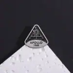 Pièce de décoration en forme de logo Apollo 1969, inspirée de la mission spatiale, posée sur une surface blanche avec un fond noir.
