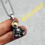 Collier avec pendentif d'astronaute en métal argenté et boule dorée, inspiré de l'espace et de l'exploration spatiale.