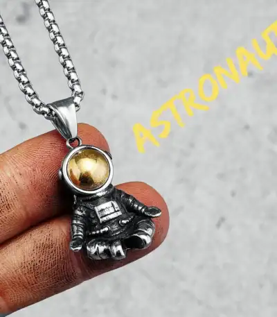 Collier avec pendentif d'astronaute en métal argenté et boule dorée, inspiré de l'espace et de l'exploration spatiale.