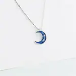 Pendentif en forme de lune bleue avec étoiles, suspendu à une chaîne fine.