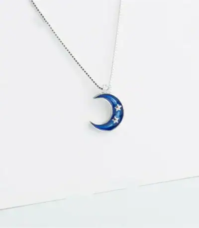 Pendentif en forme de lune bleue avec étoiles, suspendu à une chaîne fine.