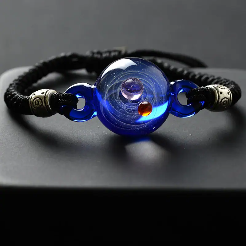 Bracelet en verre avec sphère centrale représentant un univers cosmique, orné de perles métalliques et de verre bleu foncé, idéal pour la décoration ou comme accessoire scientifique.