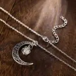Pendentif lune et étoile en argent avec détails délicats, suspendu à une chaîne fine, posé sur une surface en bois.