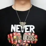 Pendentif scientifique en forme de crâne et de poing fermé avec inscription "BOSS" en lettres dorées, porté avec une chaîne en métal argenté.