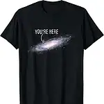 T-shirt galaxie avec texte "You're Here" en blanc sur fond noir, représentant une galaxie spirale avec un message humoristique et cosmique.