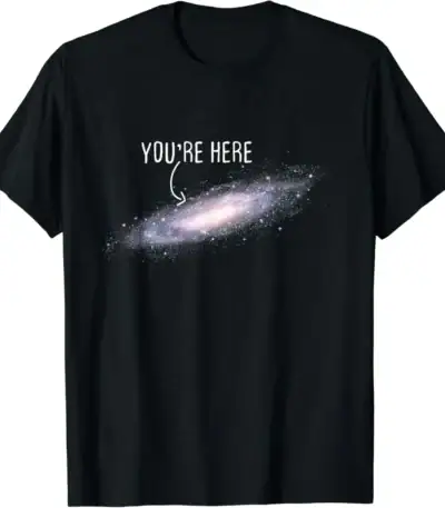 T-shirt galaxie avec texte "You're Here" en blanc sur fond noir, représentant une galaxie spirale avec un message humoristique et cosmique.