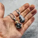 Pendentifs astronautes en métal argenté, suspendus à une chaîne, posés sur une main sale. Idéal pour les amateurs de science et d'astronomie.