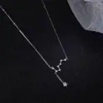 Collier délicat avec pendentif en forme de constellation étoile, en argent, suspendu à une fine chaîne, posé sur un fond noir avec un tissu en maille.