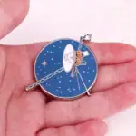 Une broche représentant une station spatiale avec antennes et panneaux solaires, idéale pour les amateurs d'astronomie et de décoration scientifique.