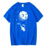 T-shirt bleu avec design d'astronaute suspendu à la lune, ambiance spatiale ludique et originale.