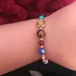 Bracelet en perles multicolores avec un charm en or, porté au poignet.