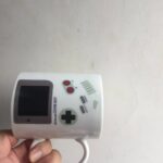 Console de jeu portable rétro blanche avec écran, boutons rouges et contrôles, idéale pour collectionner ou décorer un espace gaming.