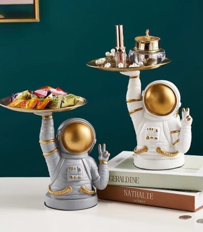 Figurine d'astronaute en céramique blanche et dorée, utilisée comme décoration, tenant un plateau avec des objets de décoration et des bonbons, style moderne et original.