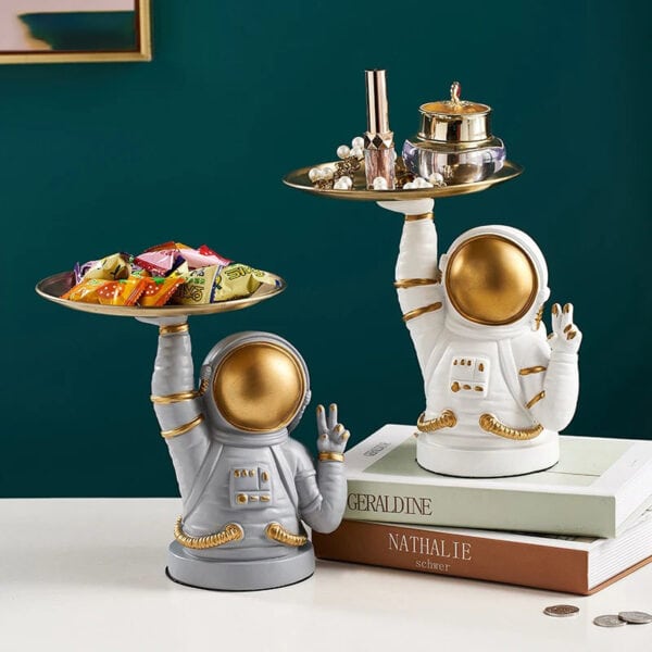 Figurine d'astronaute en céramique blanche et dorée, utilisée comme décoration, tenant un plateau avec des objets de décoration et des bonbons, style moderne et original.