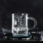Verre à mesurer en verre contenant un liquide en ébullition, placé sur une plaque de cuisson à gaz, illustrant un objet scientifique pour la décoration ou l'étude.
