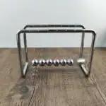 Pendulette de Newton en métal brillant avec six sphères suspendues, illustrant la conservation de l'énergie et la physique newtonienne.