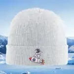 Casquette en laine blanche avec broderie d'un petit astronaute sur une fusée, idéale pour les amateurs de science et d'exploration spatiale.