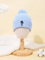 Bonnet en laine bleu clair avec un petit personnage scientifique brodé, orné d’un pompon en haut. Parfait pour les amateurs de science et de mode hivernale.