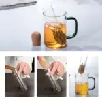 Tasse de thé en verre avec infuseur, contenant du thé infusé, sur fond blanc.