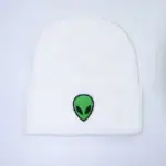 Casquette blanche avec logo d'alien vert et noir, style streetwear tendance.