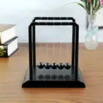 Boule de Newton en bois noir, objet de décoration scientifique, idéal pour les amateurs de physique et de design moderne, à poser sur un bureau ou une étagère.