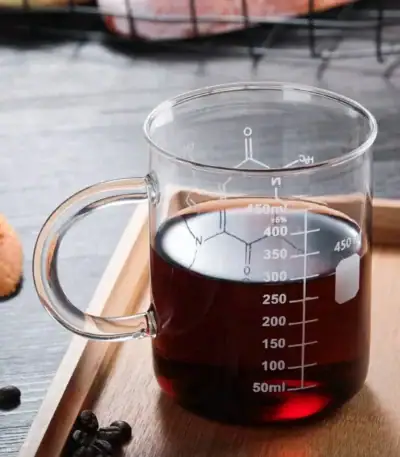 Tasse de laboratoire en verre contenant un liquide foncé, graduée pour mesurer précisément le volume, idéale pour expériences scientifiques ou décoration thématique.