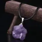 Pendentif en cristal d'améthyste brut suspendu à un cordon noir, idéal pour la décoration ou le port.