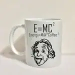 Tasse blanche avec la formule E=MC², associée à "Energy=Milk*Coffee²" et un dessin humoristique d'Einstein avec la langue sortie, illustrant un mélange amusant de science et de café.