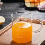 Verre de chimie en verre transparent rempli d'un liquide orange, posé sur une planche en bois, avec des fruits en arrière-plan.