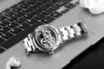Montre mécanique avec mouvement visible, bracelet en acier inoxydable, posée sur un clavier d'ordinateur.