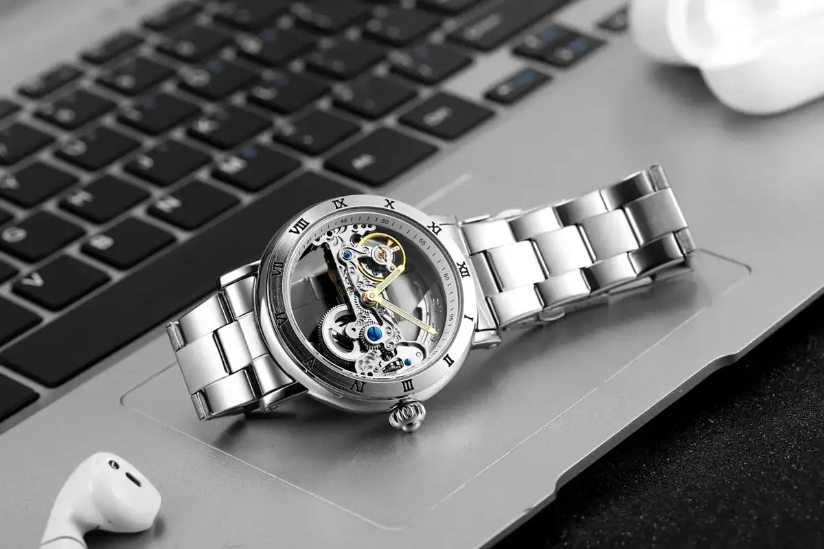 Montre mécanique avec mouvement visible, bracelet en acier inoxydable, posée sur un clavier d'ordinateur.