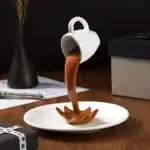 Tasse à café originale en forme de seringue, avec liquide chocolaté coulant dans une assiette, idéale pour une décoration de cuisine ou un cadeau insolite.
