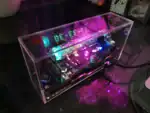 Panneau d'affichage électronique LED dans un boîtier transparent, affichant des chiffres lumineux en bleu et vert, avec des composants électroniques visibles à l'intérieur.