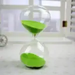 Horloge de sable en verre avec sable vert, symbole de la mesure du temps, idéale pour la décoration scientifique ou éducative.