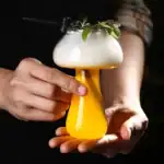Verre de cocktail scientifique avec mousse, garniture verte et décoration de laboratoire, parfait pour une décoration originale ou un événement thématique scientifique.