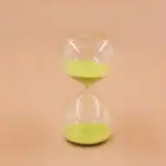 Sablier en verre transparent avec sable vert, symbole de temps et de patience, idéal pour la décoration scientifique ou comme objet de collection.