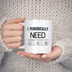 Tasse blanche avec message "I Periodically NEON" et symboles d'éléments chimiques, tenue par une personne en pull beige, sur fond neutre.