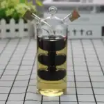Vase en verre transparent avec spirale noire à l'intérieur, contenant un liquide jaune clair, décoratif et scientifique, avec bouchons en liège sur le haut.