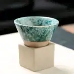 Petit pot en céramique vert avec effet marbré, posé sur un socle blanc, idéal pour la décoration scientifique ou botanique.