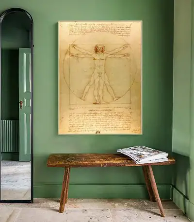 Reproduction du célèbre dessin de Léonard de Vinci, représentant l'homme de Vitruve avec ses proportions idéales, affiché sur un mur vert dans une pièce élégante.