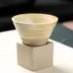 Vase en céramique beige avec finition lisse, posé sur un socle en béton blanc, idéal pour la décoration intérieure ou comme pièce de collection scientifique.