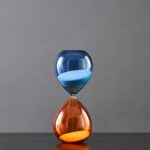 Pendentif en forme de sablier avec sable bleu et orange, symbolisant le temps et la science, parfait pour la décoration ou comme accessoire scientifique original.