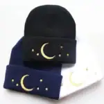 Bonnet en laine avec motif lune et étoiles dorées, disponible en noir, bleu marine et blanc. Parfait pour un style cosy et tendance, idéal pour l'hiver ou comme accessoire original.