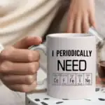 Mug blanc avec texte "I PERIODICALLY NEED" et tableau périodique illustrant des éléments chimiques, parfait pour les amateurs de science et de chimie.